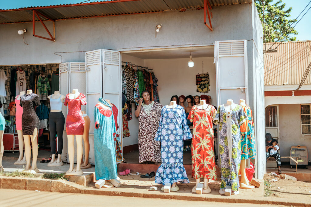 A woman standing at the door of her garment store and talking using her mobile phone. 