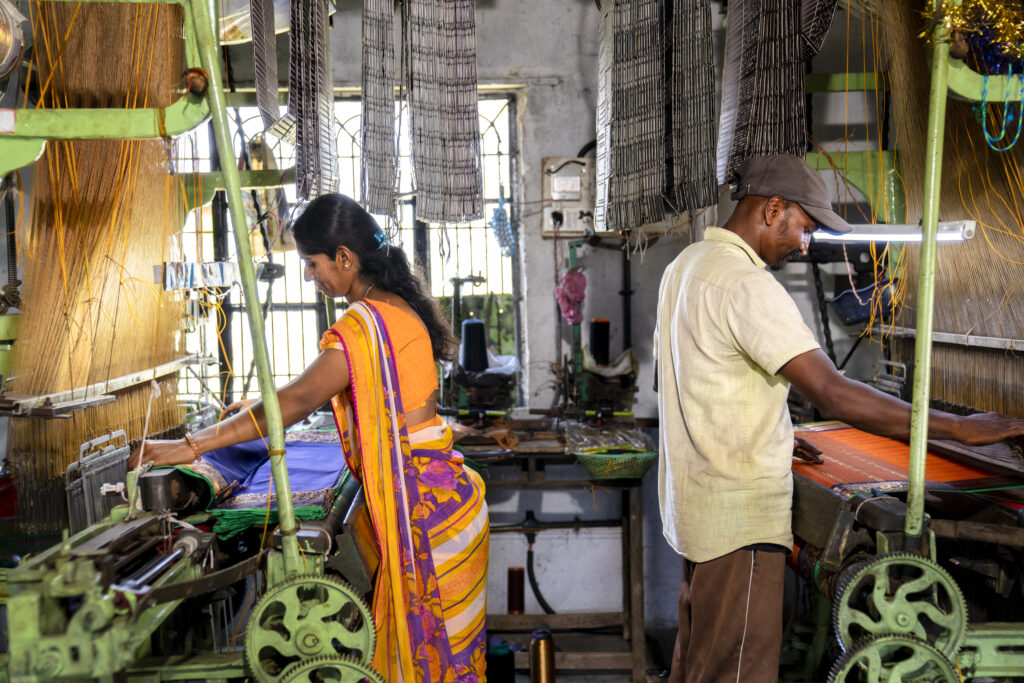 A man and a woman operating power looms in a workshop.