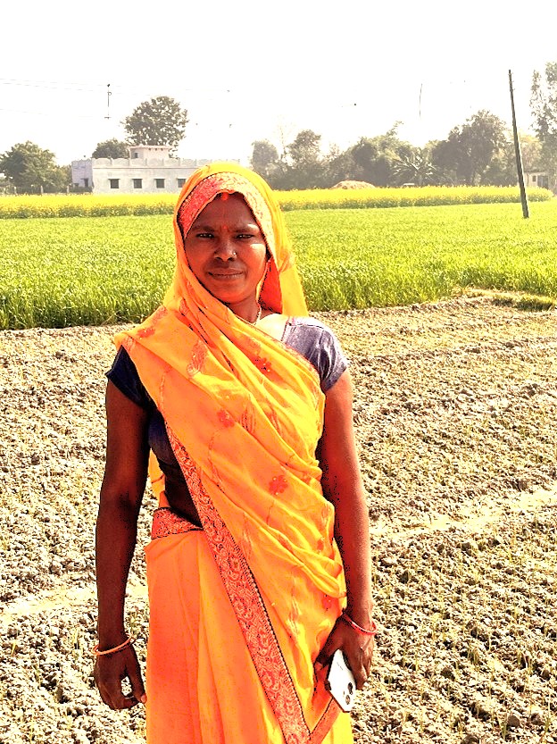 A woman standing in a farm with a mobile phone in her hand. 